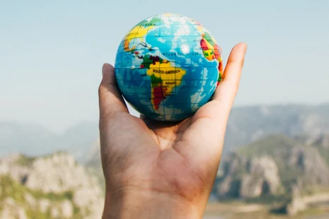 kleiner Globus in einer Hand vor einer Berglandschaft