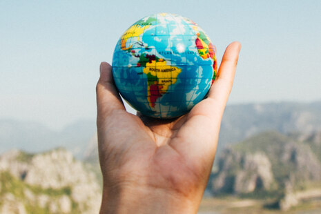 kleiner Globus in einer Hand vor einer Berglandschaft