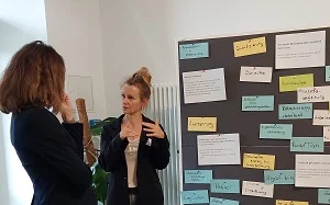 zwei Personen diskutieren vor Pinnwand