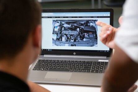 Zwei Personen sitzen vor einem Laptop. Auf dem Bildschirm ist ein Motor erkennbar.