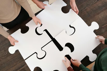 Vier Menschen halten vier große Puzzleteile aneinander.