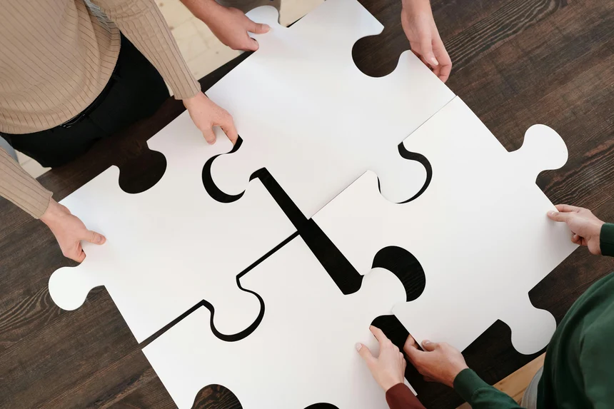 Vier Menschen halten vier große Puzzleteile aneinander.