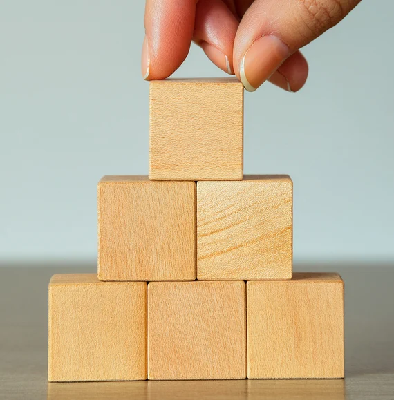 Hände stapeln eine Pyramide aus Holzwürfeln