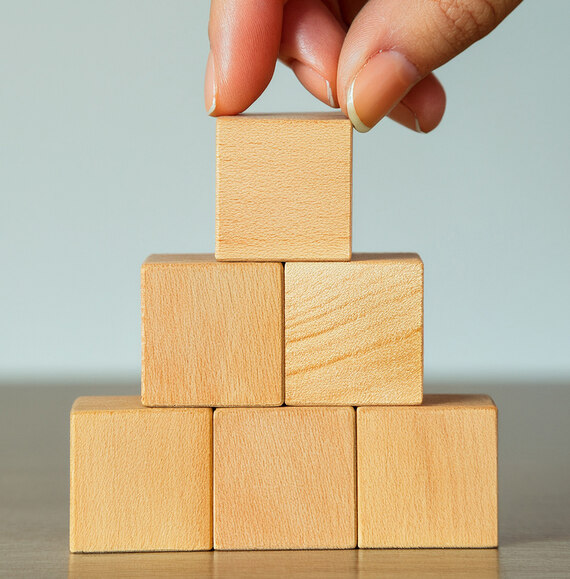 Hände stapeln eine Pyramide aus Holzwürfeln